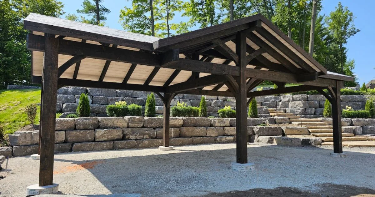 Timber pavilion structure set against a landscaped stone wall